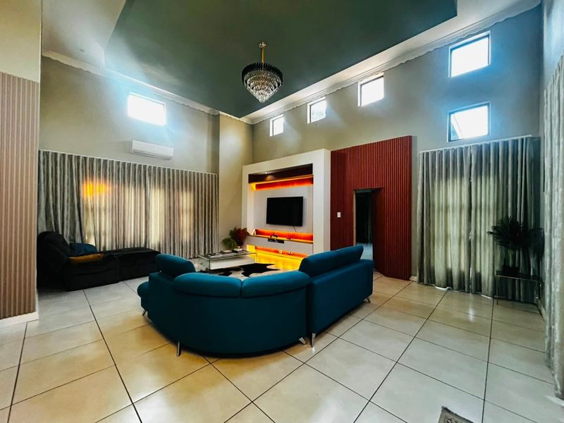 Spacious living room featuring high ceilings, tiled flooring, a modern built-in media unit with integrated lighting, and large windows with floor-to-ceiling curtains.