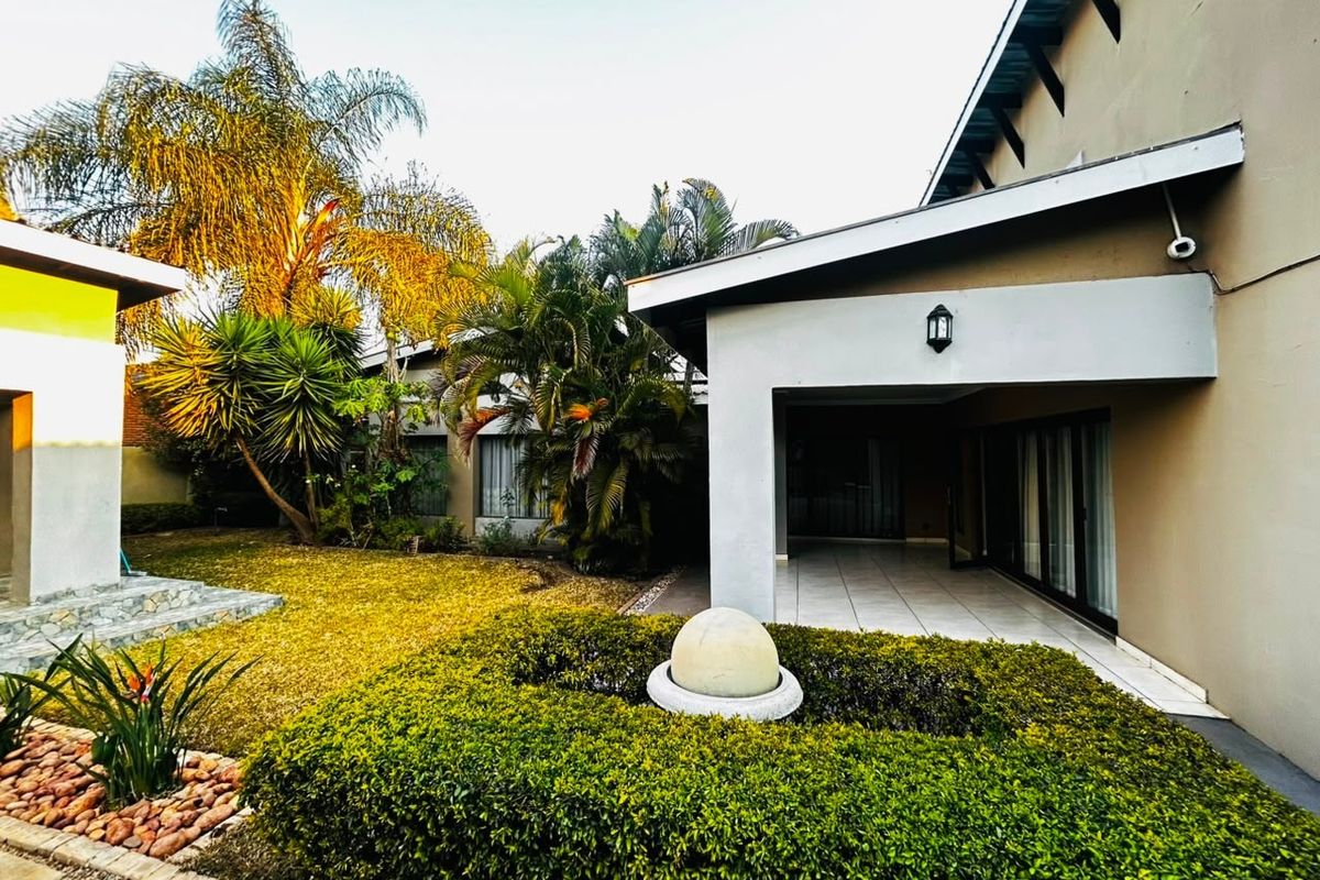 A well-maintained rear exterior featuring a covered patio with tiled flooring, sliding glass doors, and a landscaped garden with a central stone water feature.