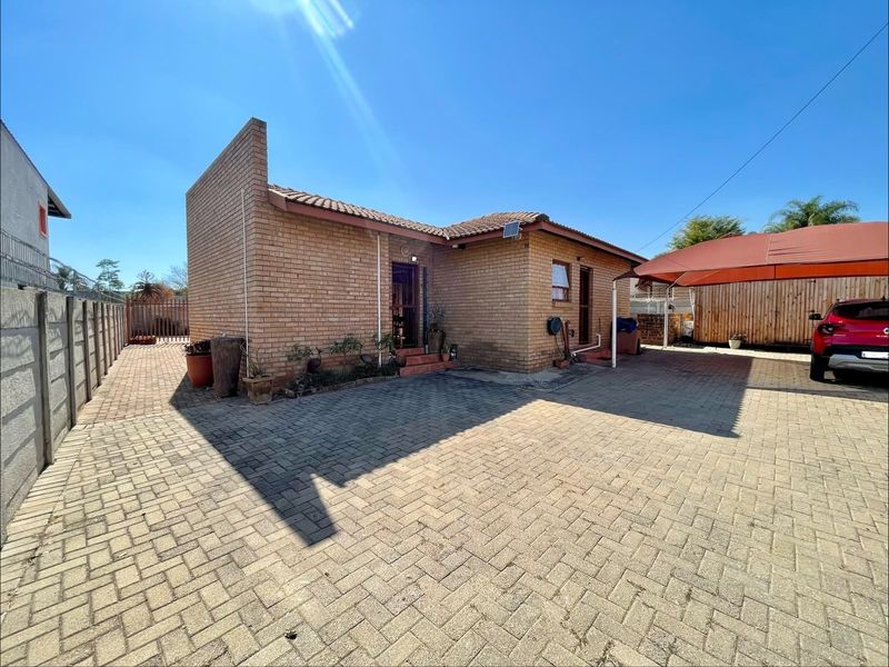 Front exterior view of a face brick house featuring a paved driveway, carport, and perimeter boundary wall.