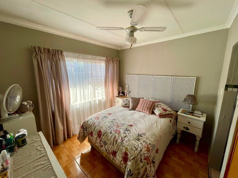 A well-lit bedroom featuring tiled flooring, a ceiling fan, and large windows with curtain rails, offering a comfortable and functional living space.