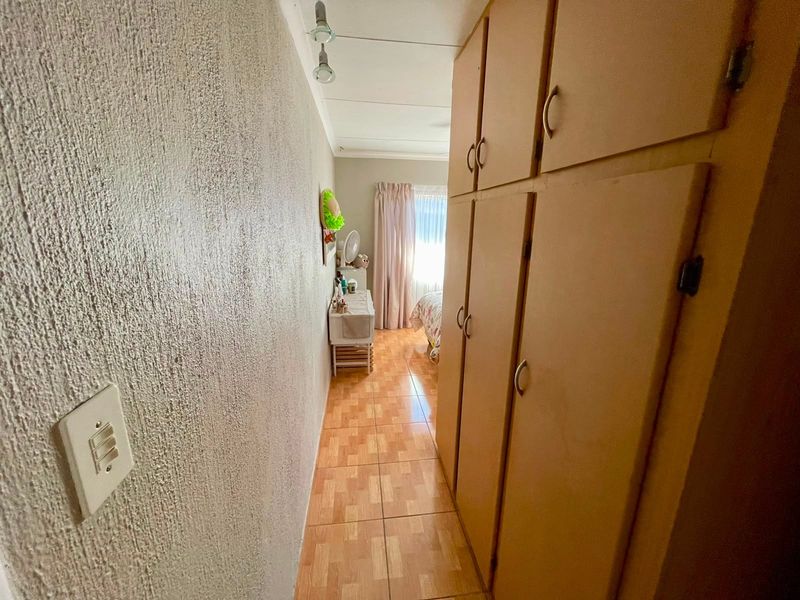 A narrow hallway featuring built-in wooden cupboards and tiled flooring, leading towards a bedroom area.