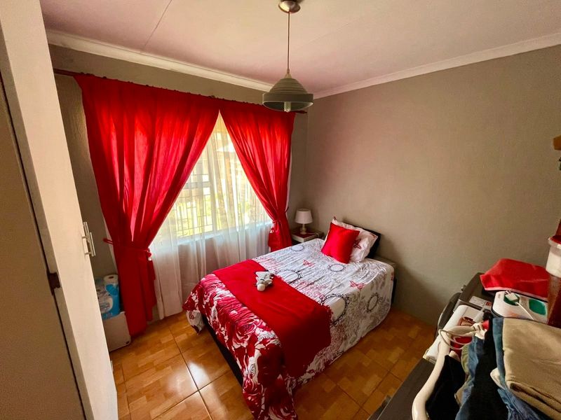 A compact bedroom featuring tiled flooring, a central pendant light, and a window fitted with security bars.