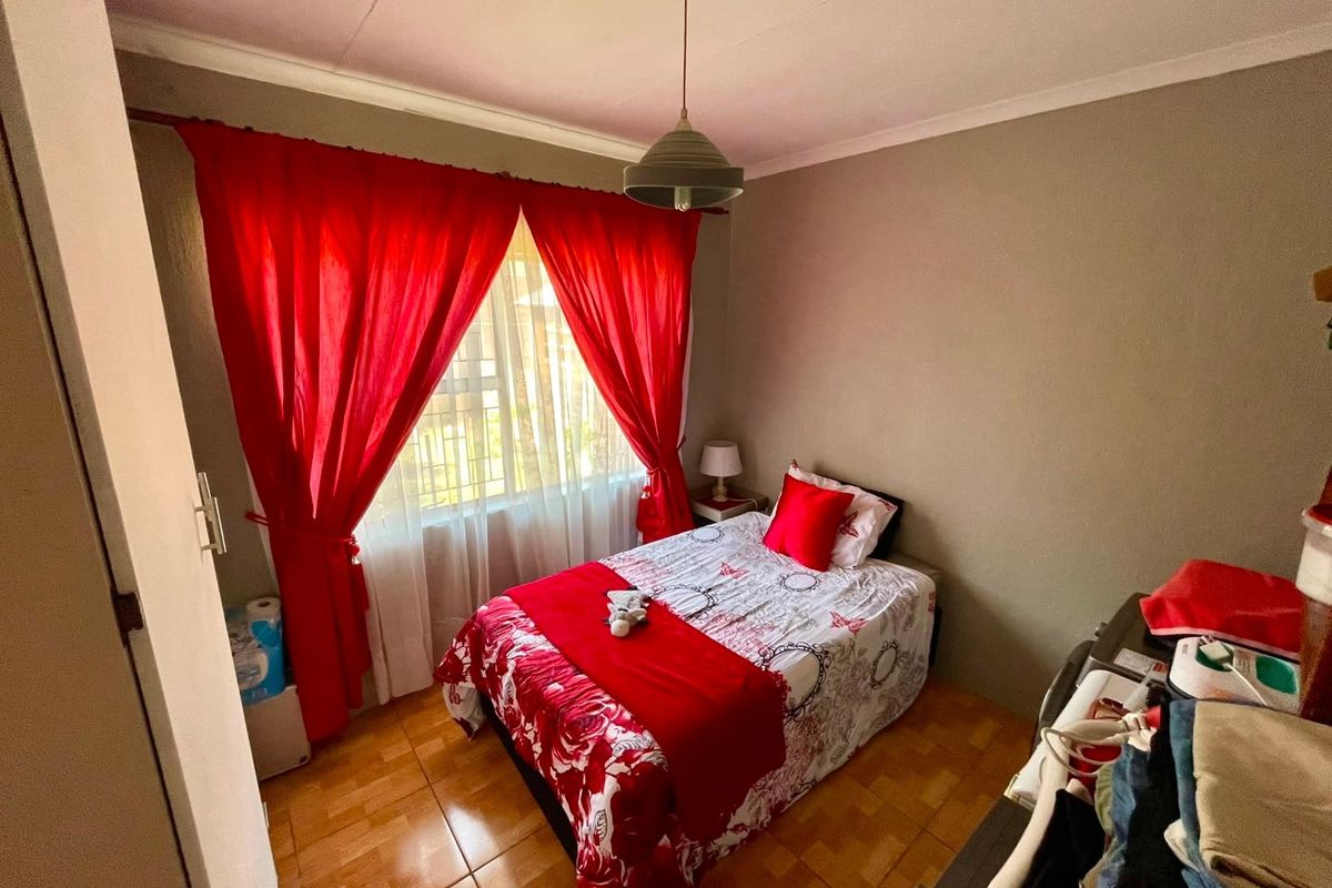 A compact bedroom featuring tiled flooring, a central pendant light, and a window fitted with security bars.