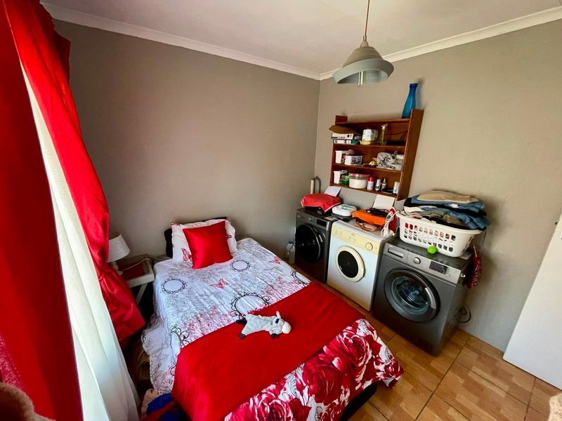 A bedroom featuring tiled flooring and cove cornicing, currently utilized as a multi-purpose space with laundry appliances integrated into the room layout.