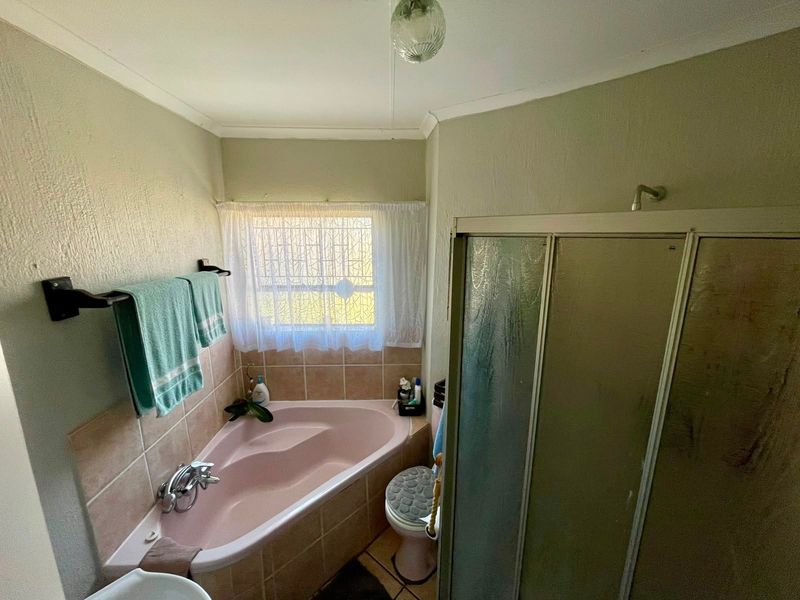 A functional bathroom featuring a corner bathtub, separate shower enclosure, and toilet, with dated finishes and neutral wall tones.