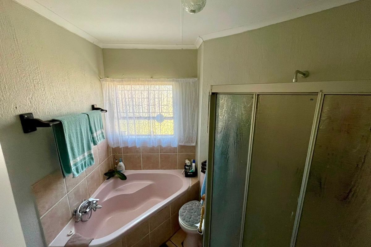 A functional bathroom featuring a corner bathtub, separate shower enclosure, and toilet, with dated finishes and neutral wall tones.