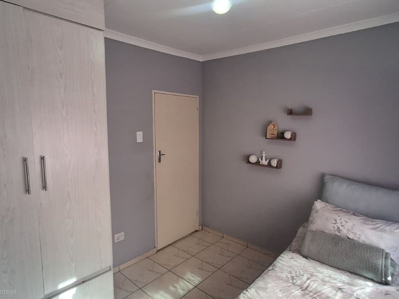 A functional bedroom featuring tiled flooring, a built-in wardrobe, and neutral grey wall finishes.