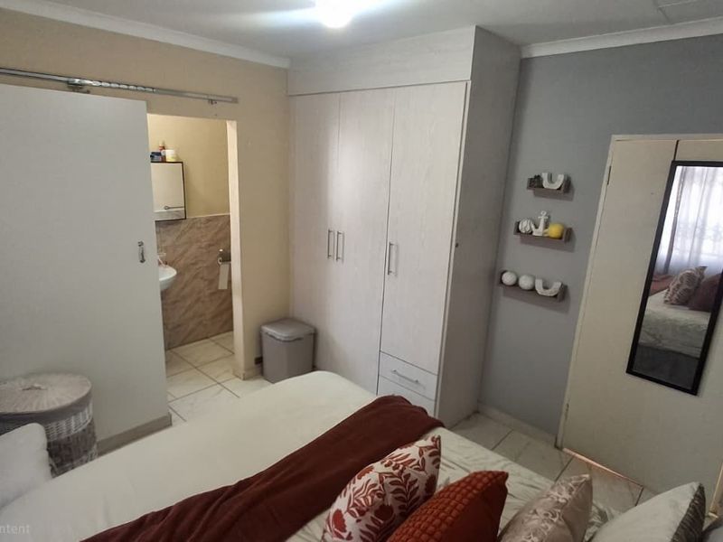 A bedroom featuring built-in cupboards and an attached en-suite bathroom with tiled flooring and neutral wall finishes.