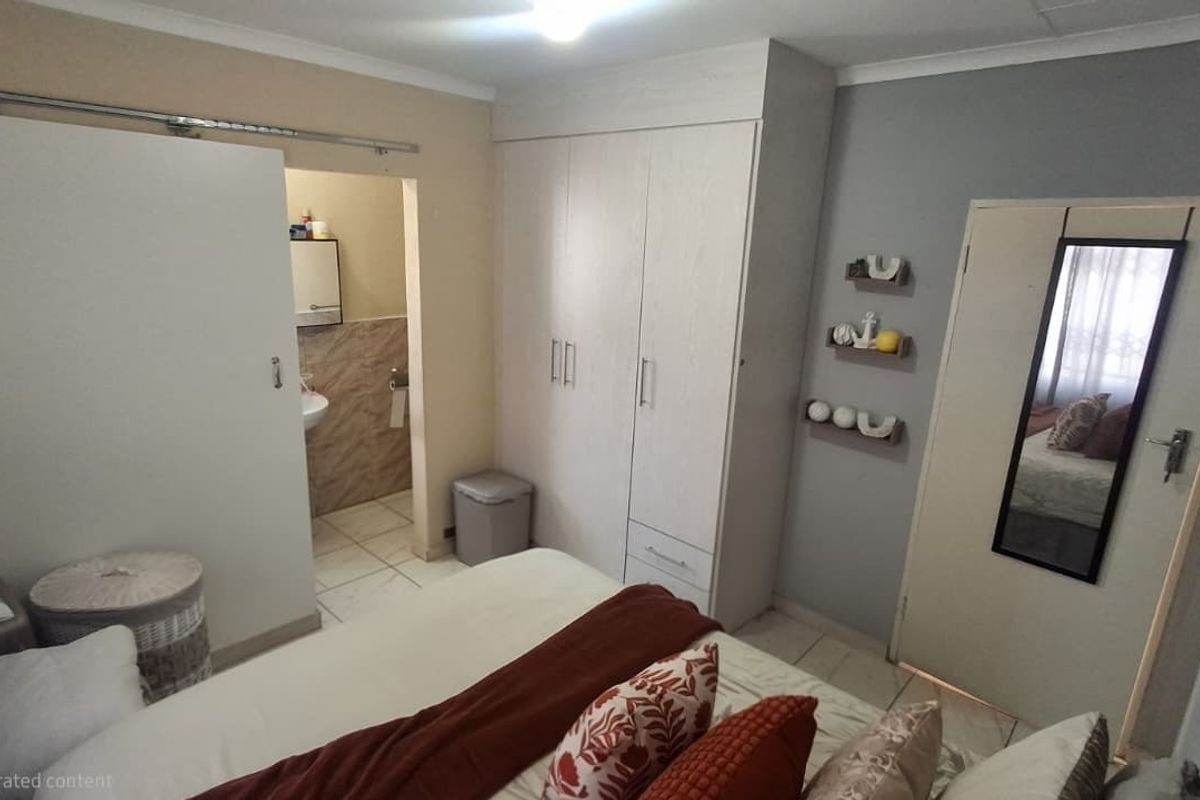 A bedroom featuring built-in cupboards and an attached en-suite bathroom with tiled flooring and neutral wall finishes.