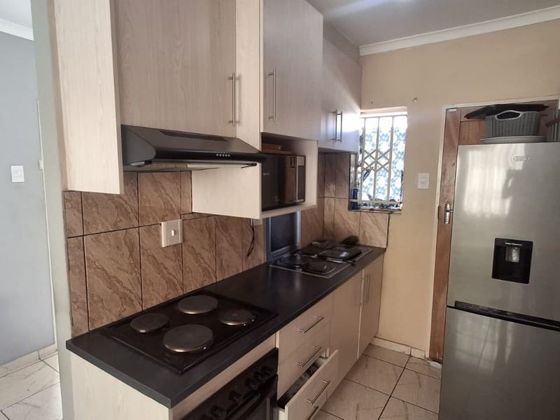A compact kitchen featuring built-in cabinetry, laminate countertops, an electric hob with extractor fan, and tiled flooring.
