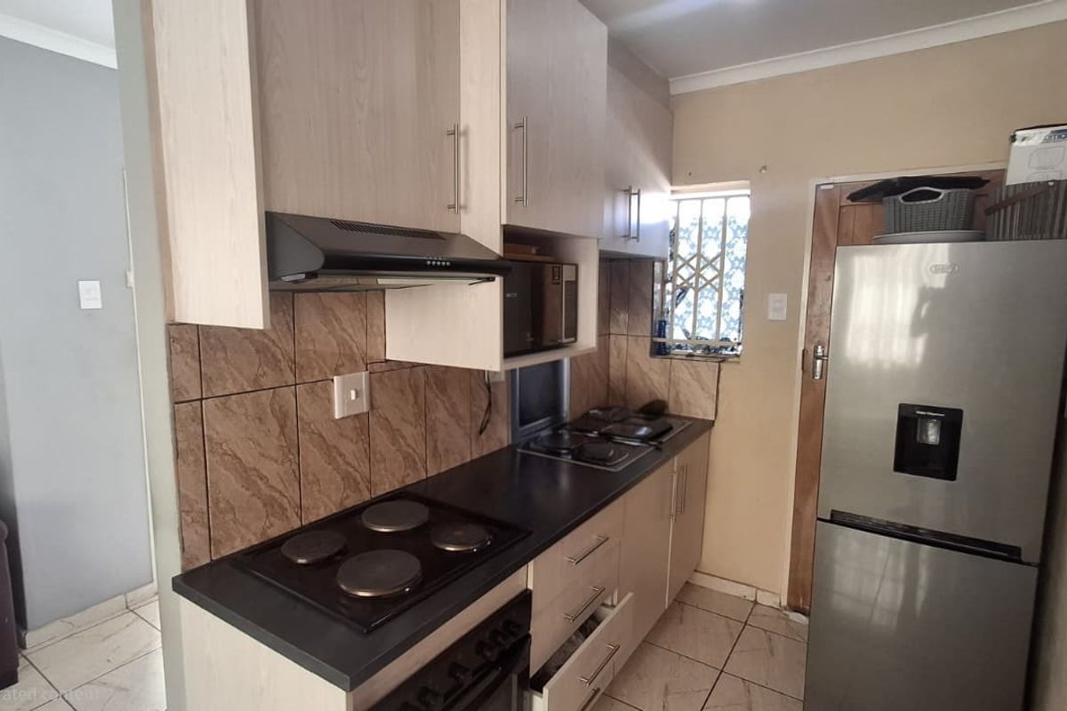 A compact kitchen featuring built-in cabinetry, laminate countertops, an electric hob with extractor fan, and tiled flooring.