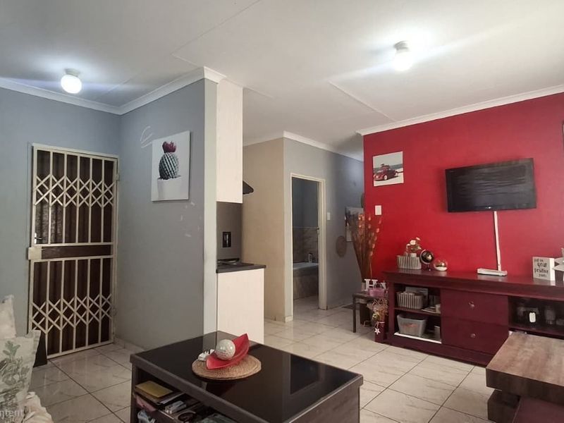 Open plan living area featuring tiled flooring, neutral and accent wall finishes, and a security gate leading to the exterior.
