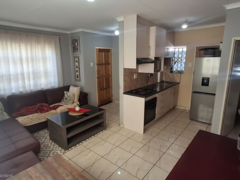 Open-plan living area featuring a functional kitchen with built-in cabinetry, electric hob, and oven, seamlessly connected to the lounge space with tiled flooring.