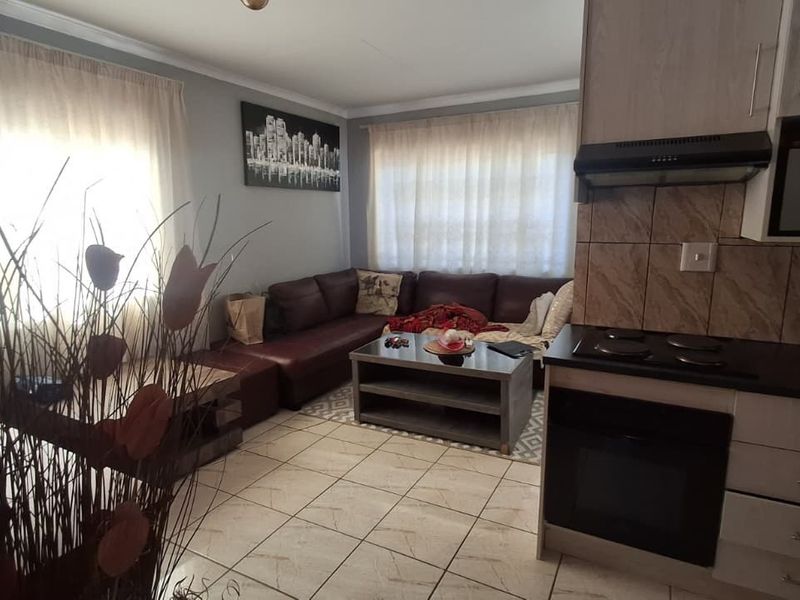 Open-plan living area featuring tiled flooring and a compact kitchen with built-in cabinetry, oven, hob, and extractor fan.