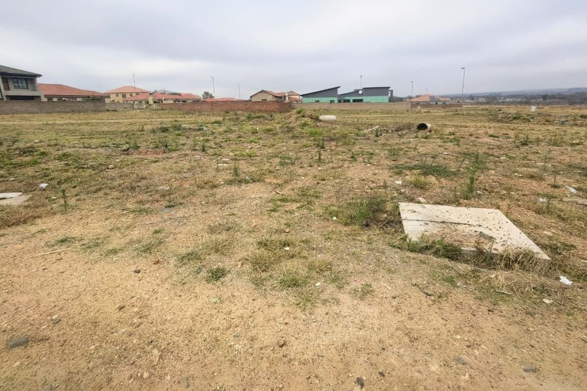 A vacant residential plot of land featuring natural ground cover and visible utility access points, situated within a developed residential estate.