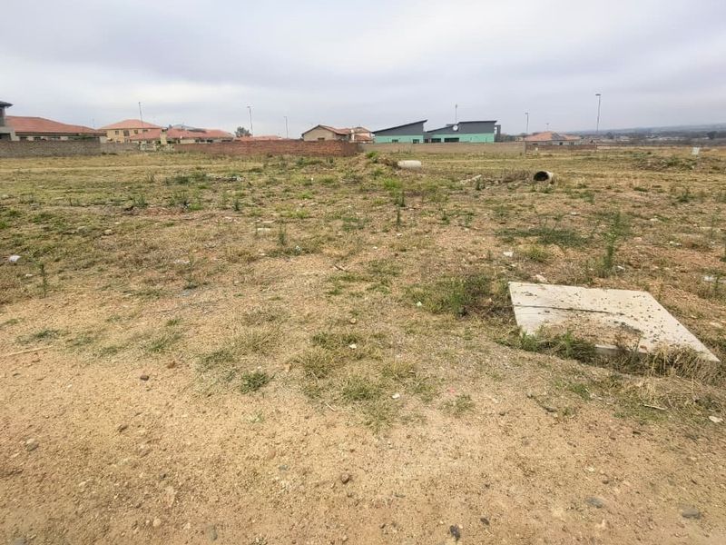 A vacant residential plot of land featuring natural ground cover and visible utility access points, situated within a developed residential estate.