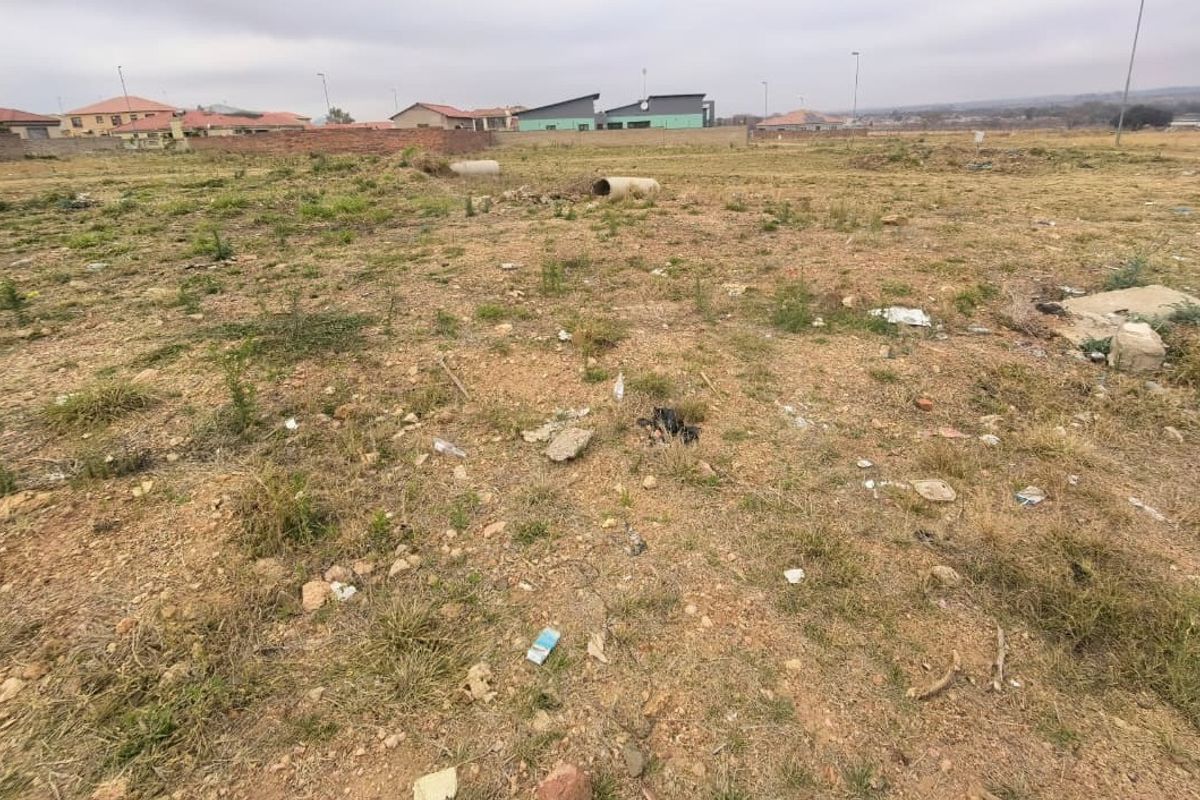 A view of a vacant residential plot of land with surrounding neighborhood development visible in the background.