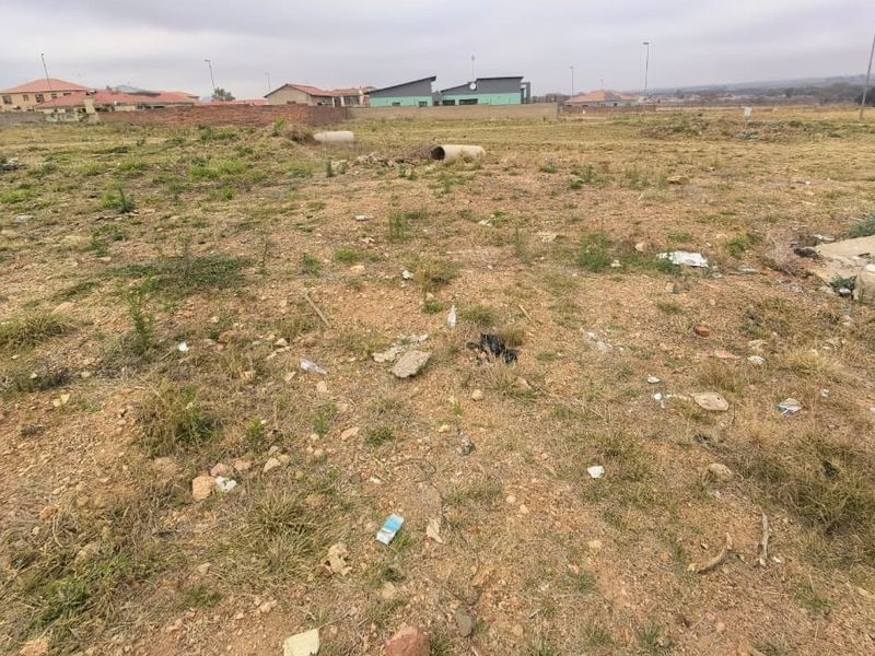 A view of a vacant residential plot of land with surrounding neighborhood development visible in the background.