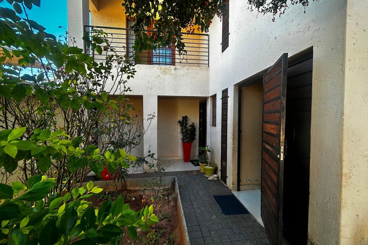 A rear courtyard area featuring a paved walkway, a small garden bed, and an upper-level balcony with metal railings.