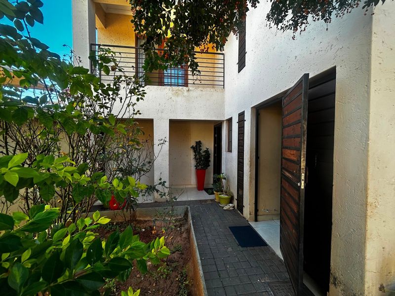 A rear courtyard area featuring a paved walkway, a small garden bed, and an upper-level balcony with metal railings.