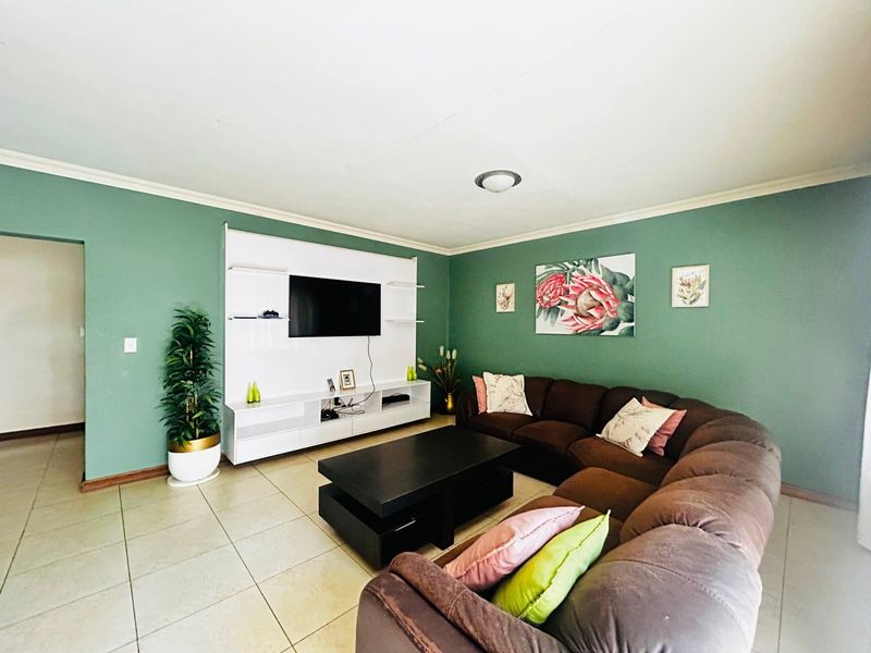 A living room featuring green painted walls, tiled flooring, and a built-in white media unit.