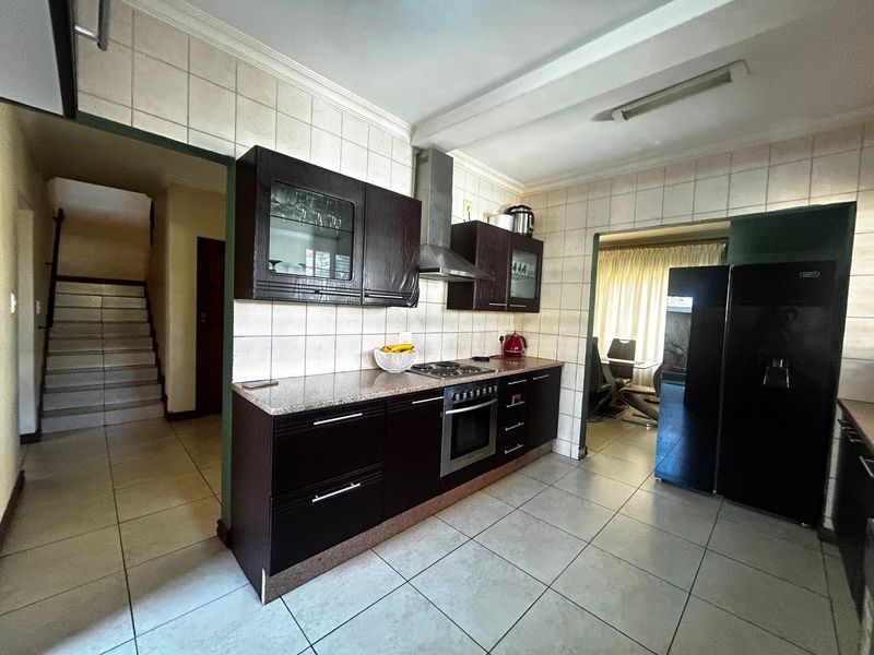 A functional kitchen featuring dark wood cabinetry, granite countertops, a built-in oven with gas hob, and tiled finishes throughout.