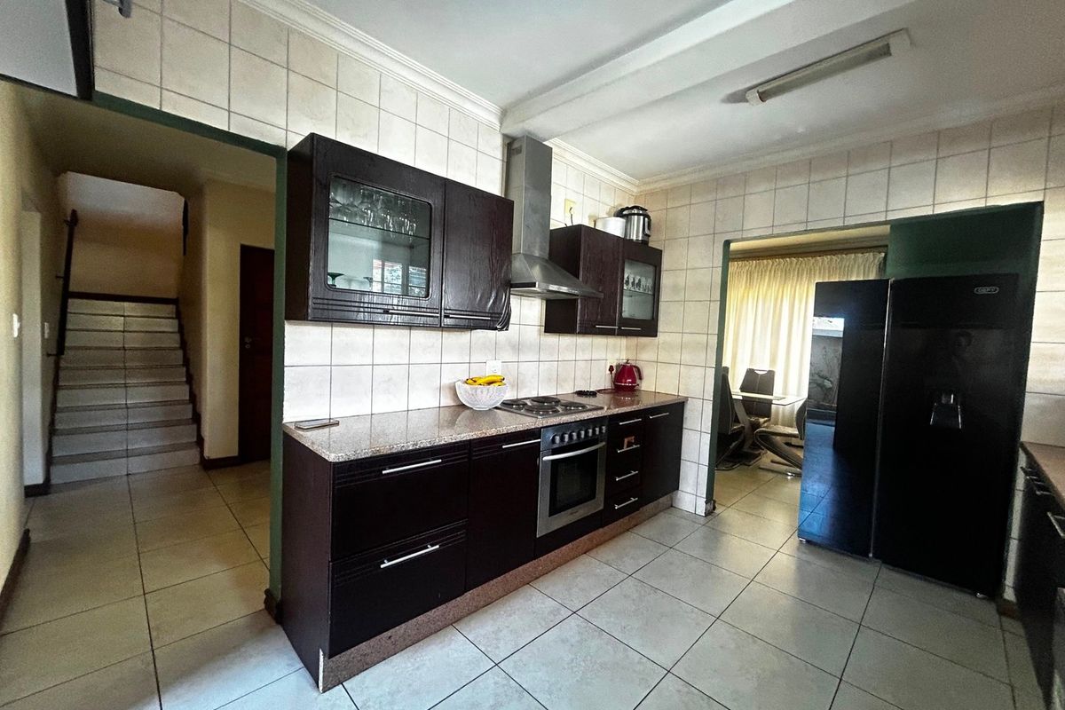 A functional kitchen featuring dark wood cabinetry, granite countertops, a built-in oven with gas hob, and tiled finishes throughout.