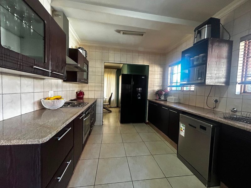 A functional kitchen featuring dark wood cabinetry, stone countertops, tiled walls, and integrated appliances, offering a practical layout for daily meal preparation.
