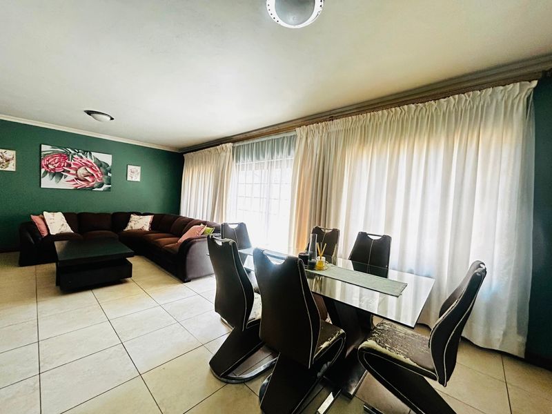 Spacious open-plan living and dining area featuring neutral tiled flooring and large windows with full-length curtains.