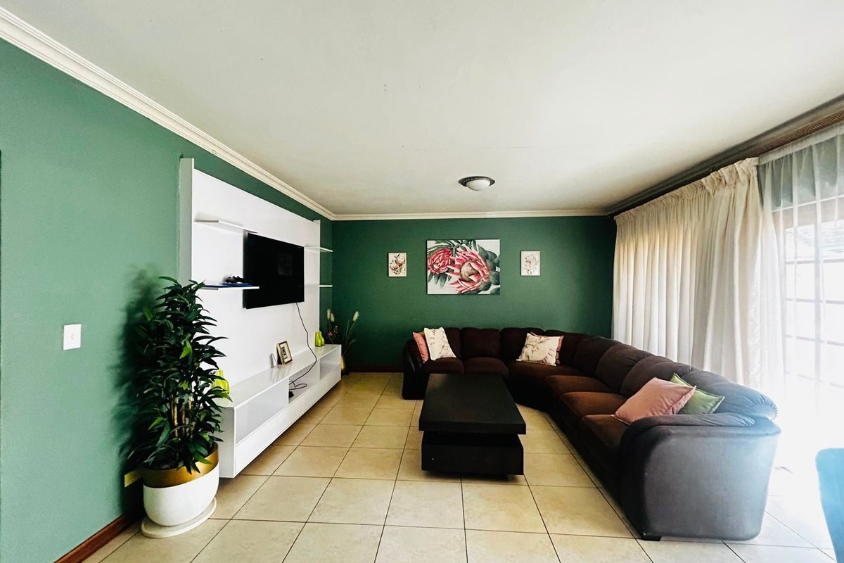 A spacious living room featuring green accent walls, ceramic tiled flooring, and a built-in media unit with integrated shelving.