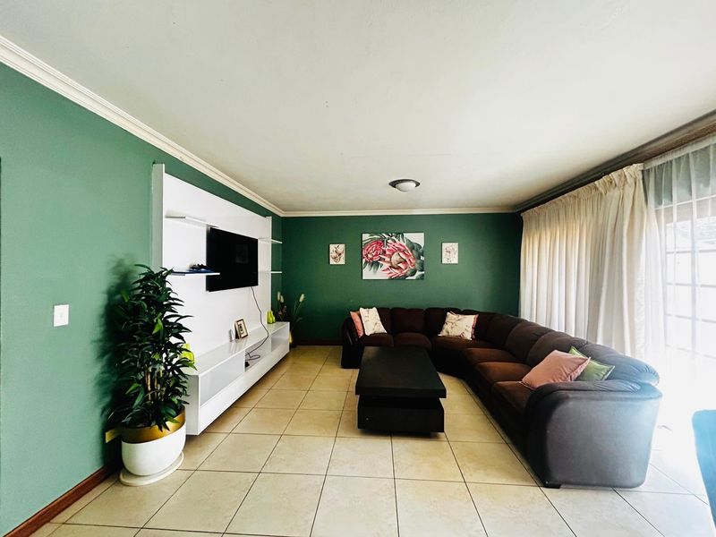 A spacious living room featuring green accent walls, ceramic tiled flooring, and a built-in media unit with integrated shelving.