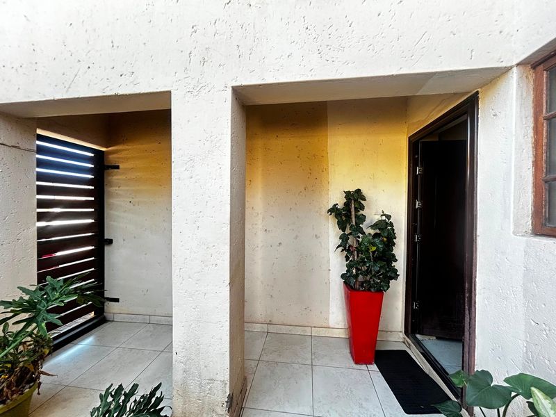 A covered entrance area featuring tiled flooring, a security gate, and a main entrance door, showing signs of wear on the exterior wall finish.