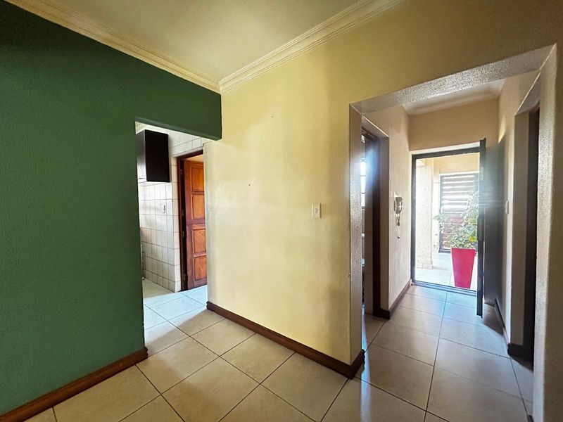 A functional hallway featuring tiled flooring, cornicing, and an intercom system, providing access to the kitchen and exterior entrance.