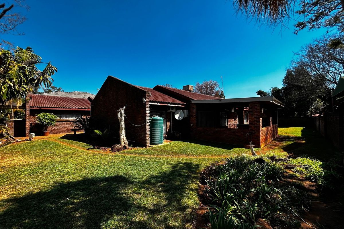 Rear view of a brick house featuring a covered patio, a water tank, and a well-maintained garden area.
