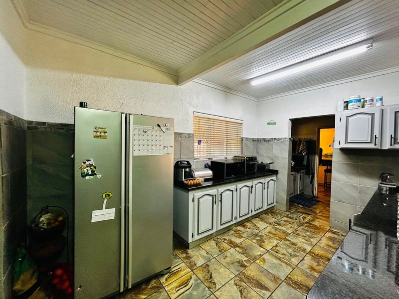 A functional kitchen featuring granite countertops, tiled flooring, and ample built-in cabinetry, with a separate scullery area visible through the doorway.