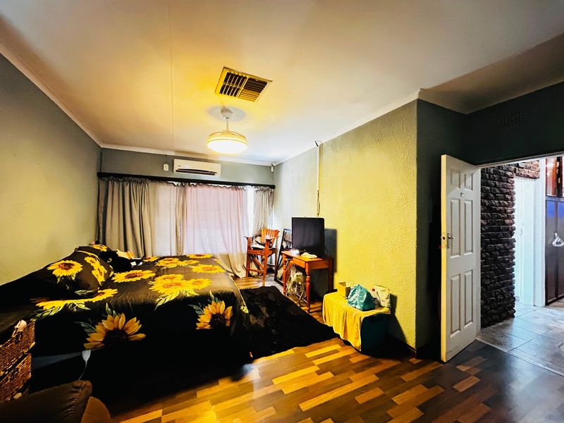 A bedroom featuring laminate flooring, an air conditioning unit, and a ceiling vent, with access to an adjacent area through a panel door.
