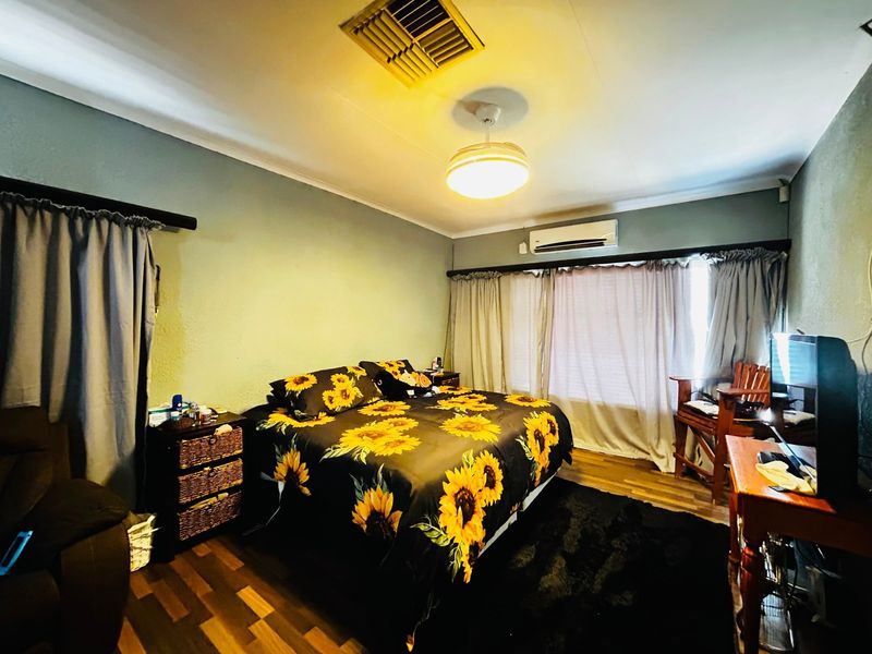 A bedroom featuring laminate flooring, a ceiling fan, and a wall-mounted air conditioning unit.
