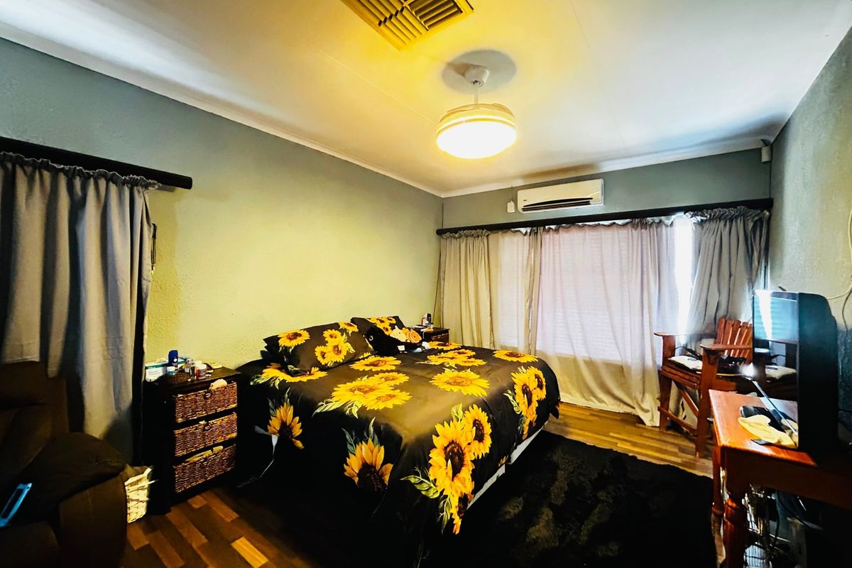 A bedroom featuring laminate flooring, a ceiling fan, and a wall-mounted air conditioning unit.
