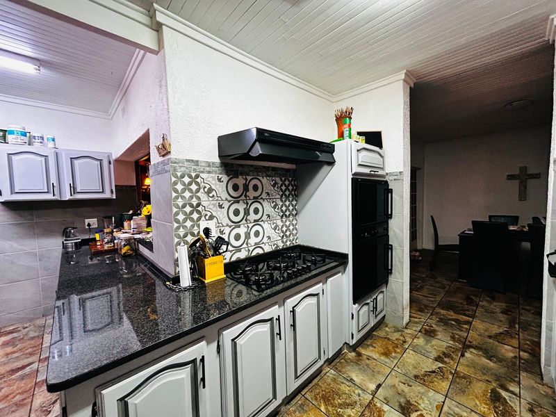 A functional kitchen featuring granite countertops, a gas hob with extractor fan, built-in oven, and decorative tiled backsplash with timber ceiling finishes.