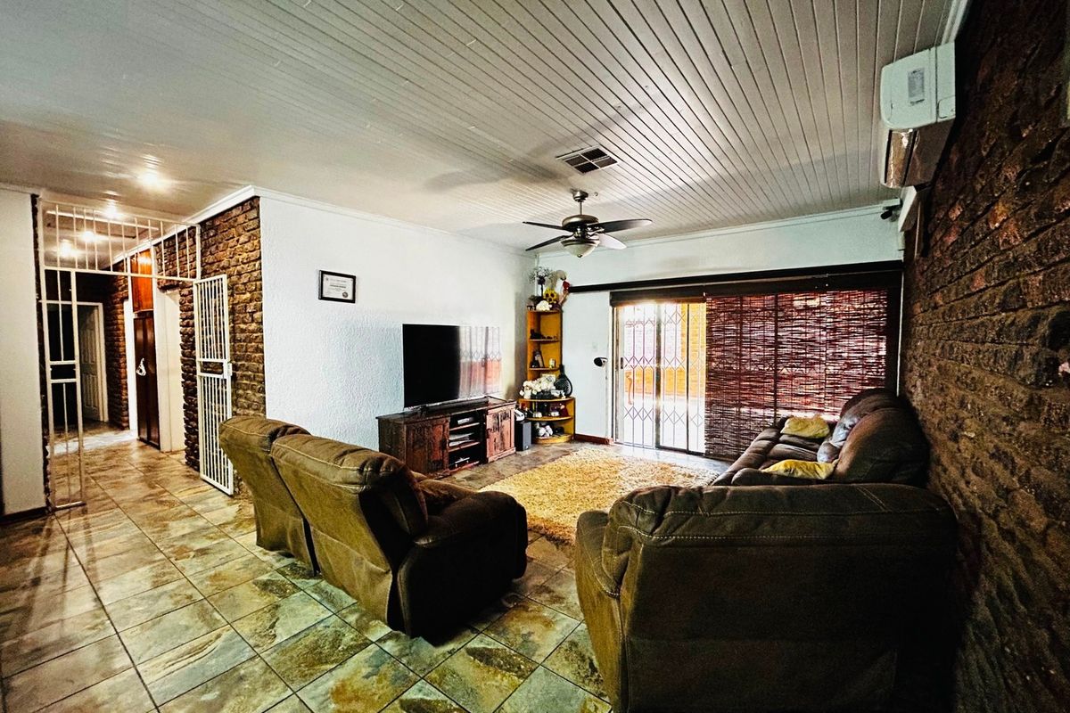 Spacious living room featuring exposed brick walls, tiled flooring, a ceiling fan, and a split-system air conditioner with access to the outdoor area.