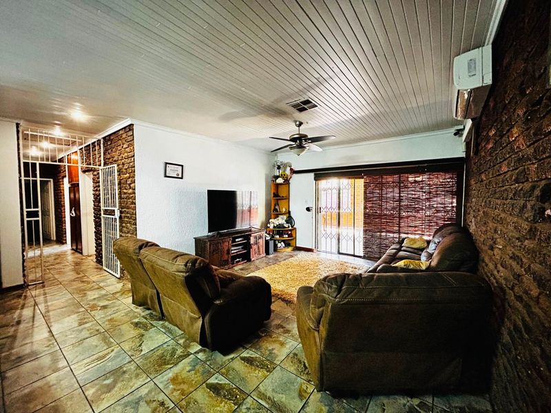 Spacious living room featuring exposed brick walls, tiled flooring, a ceiling fan, and a split-system air conditioner with access to the outdoor area.