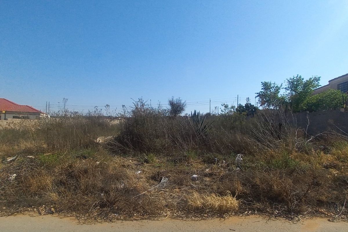 A vacant residential plot featuring overgrown vegetation and boundary walls, situated in a developed neighborhood.