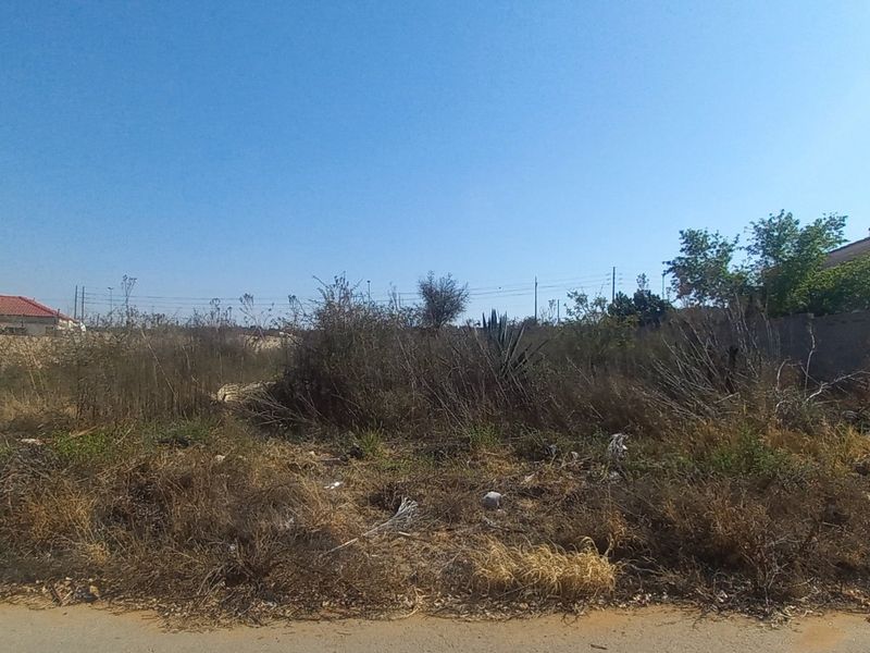 A vacant residential plot featuring overgrown vegetation and boundary walls, situated in a developed neighborhood.