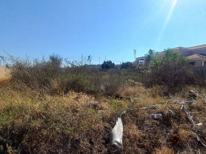 Vacant residential land featuring a perimeter wall with electric fencing, currently covered in overgrown vegetation and debris.