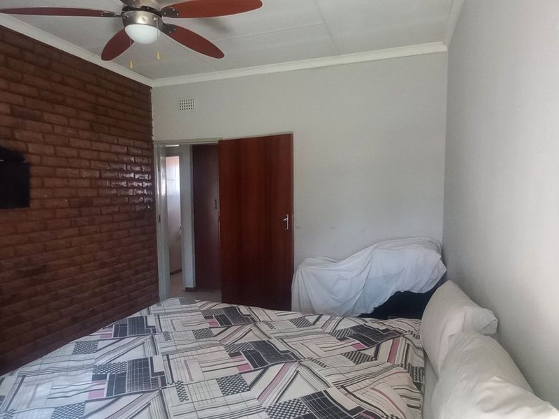 A bedroom featuring an exposed brick feature wall, ceiling fan, and neutral painted walls with a standard interior door.