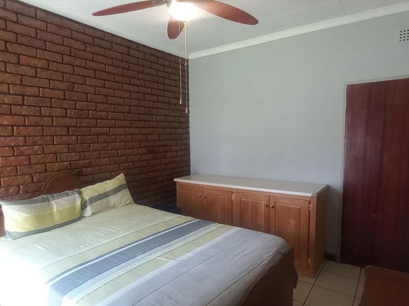 A bedroom featuring an exposed brick feature wall, tiled flooring, and a ceiling fan, offering a functional space with potential for modern updates.