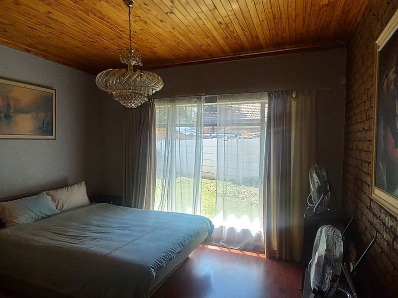 A bedroom featuring a timber ceiling, exposed brick wall, and sliding glass door providing access to the garden.