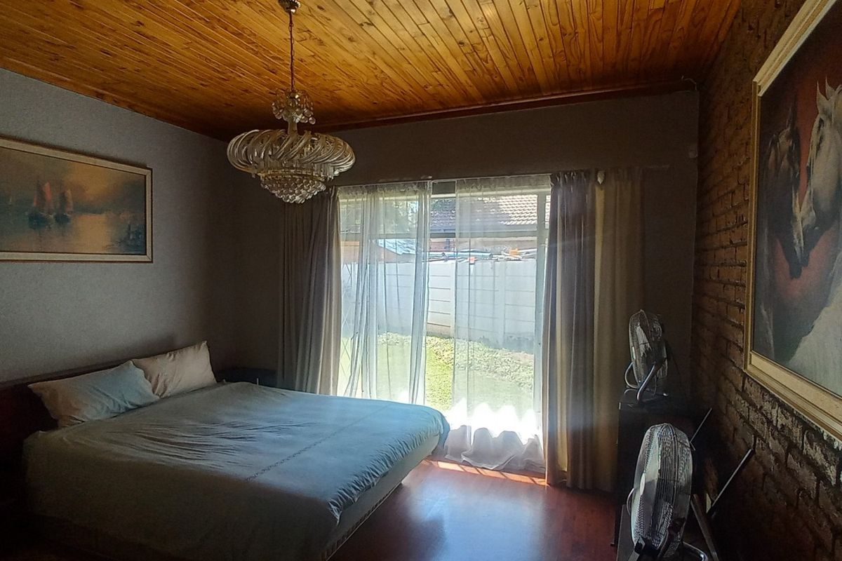 A bedroom featuring a timber ceiling, exposed brick wall, and sliding glass door providing access to the garden.