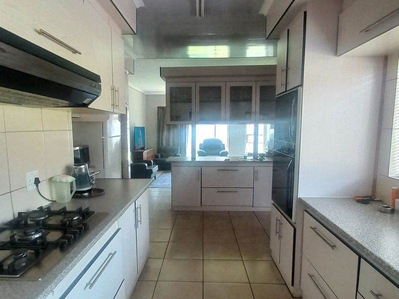 A functional kitchen featuring laminate cabinetry, a gas hob with extractor fan, built-in oven, and tiled flooring, with an open flow to the living area.