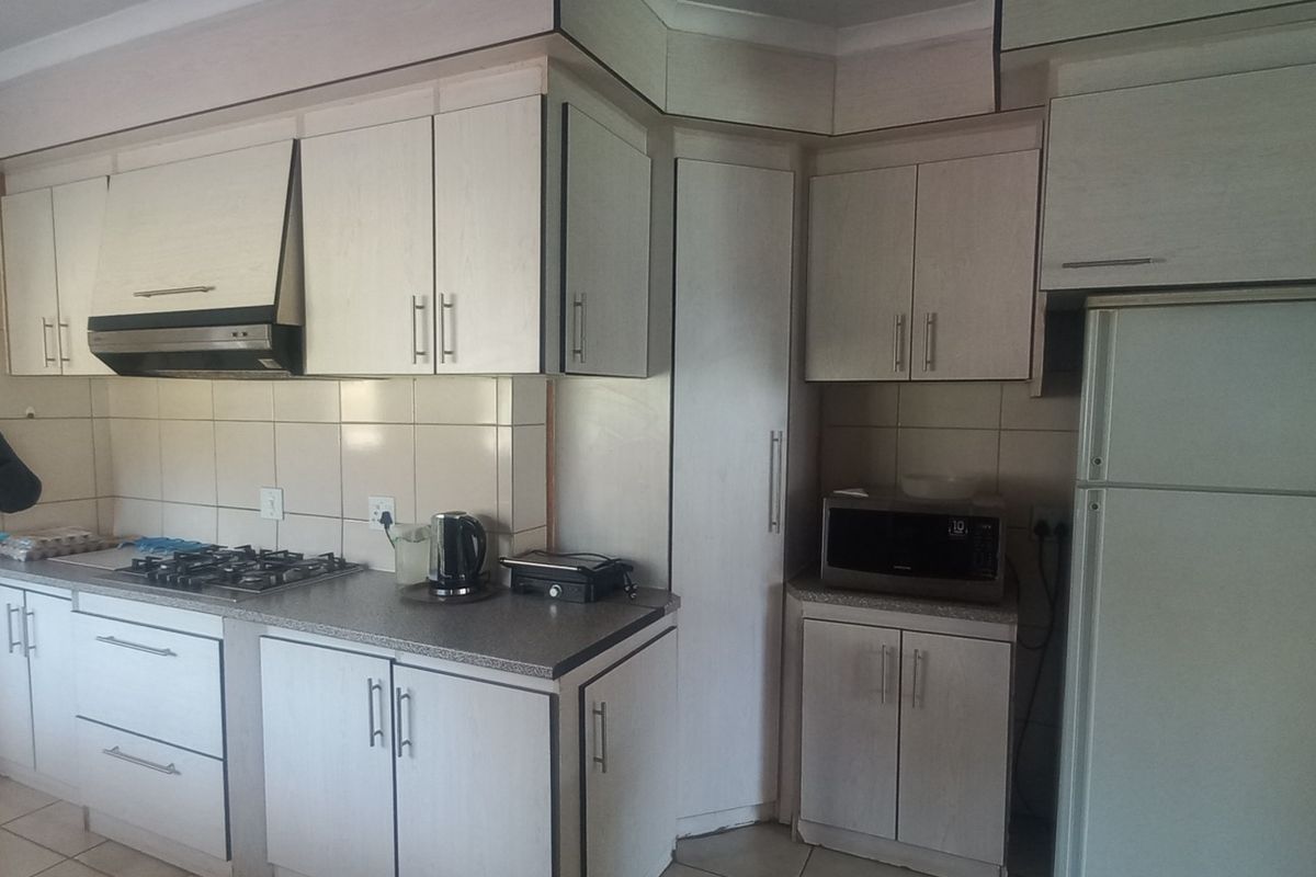 A functional kitchen featuring light-toned built-in cabinetry, a gas hob with extractor fan, tiled splashbacks, and an arched entryway leading to an adjacent space.